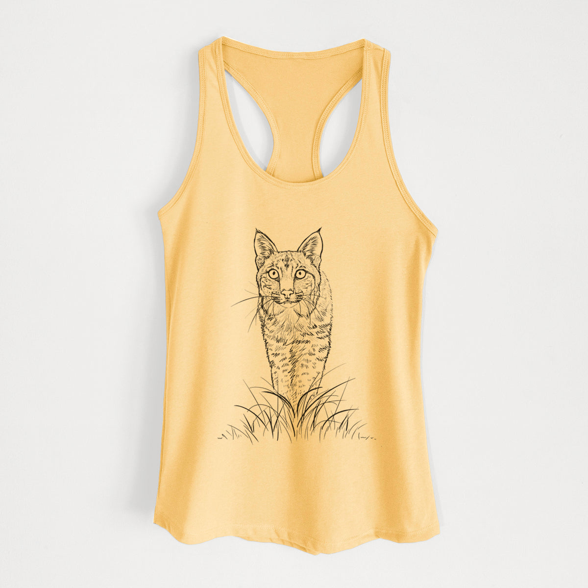Banana cream women's racerback tank top laid flat, printed with a black ink illustration of a bobcat standing in tall grass, facing forward.
