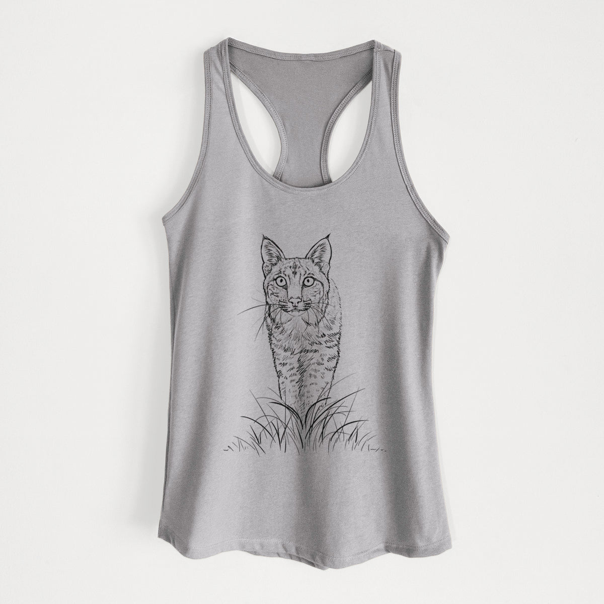 Heather grey women's racerback tank top laid flat, printed with a black ink illustration of a bobcat standing in tall grass, facing forward.