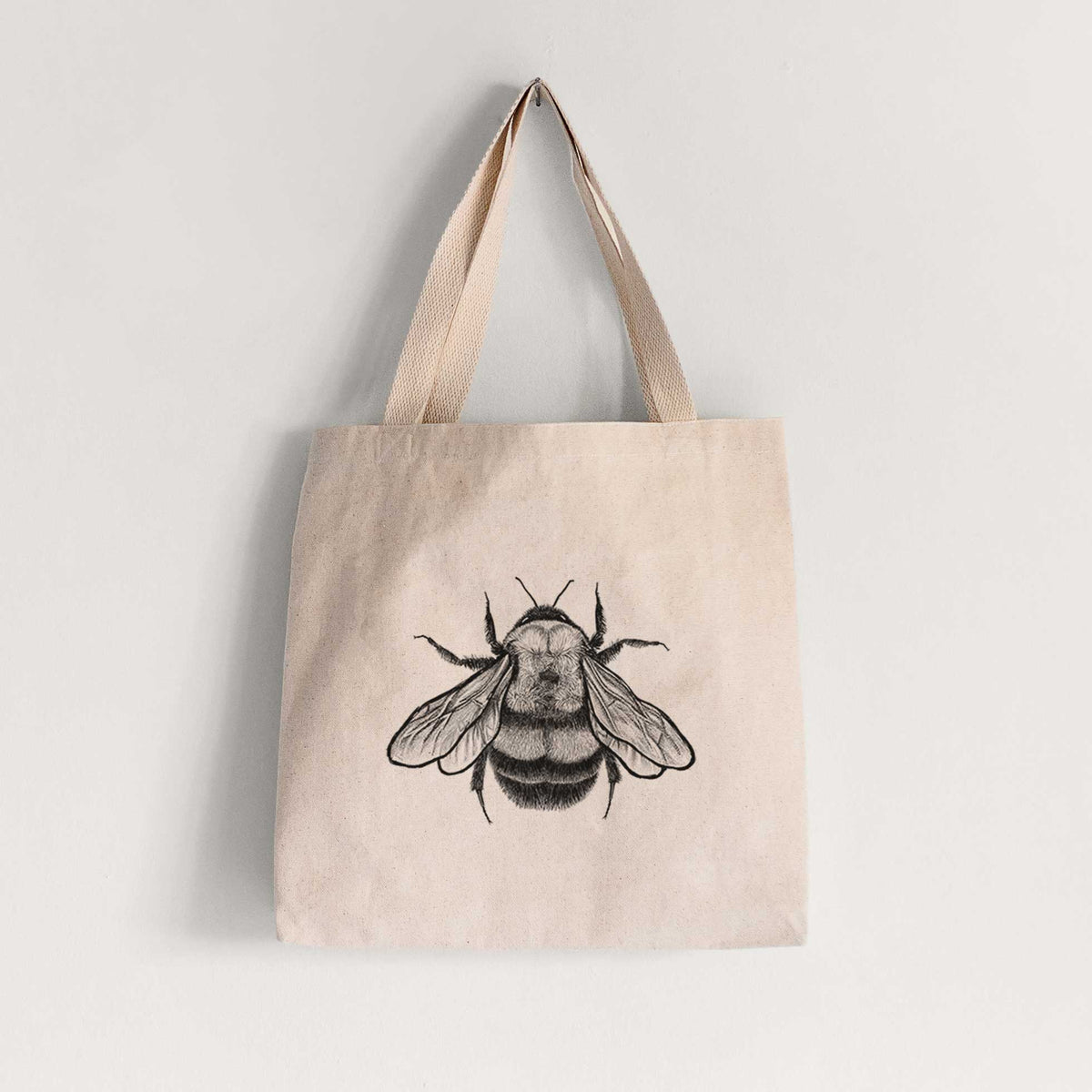 Natural canvas tote bag printed with a detailed black ink illustration of a rusty patched bumble bee with its wings spread, seen from above.