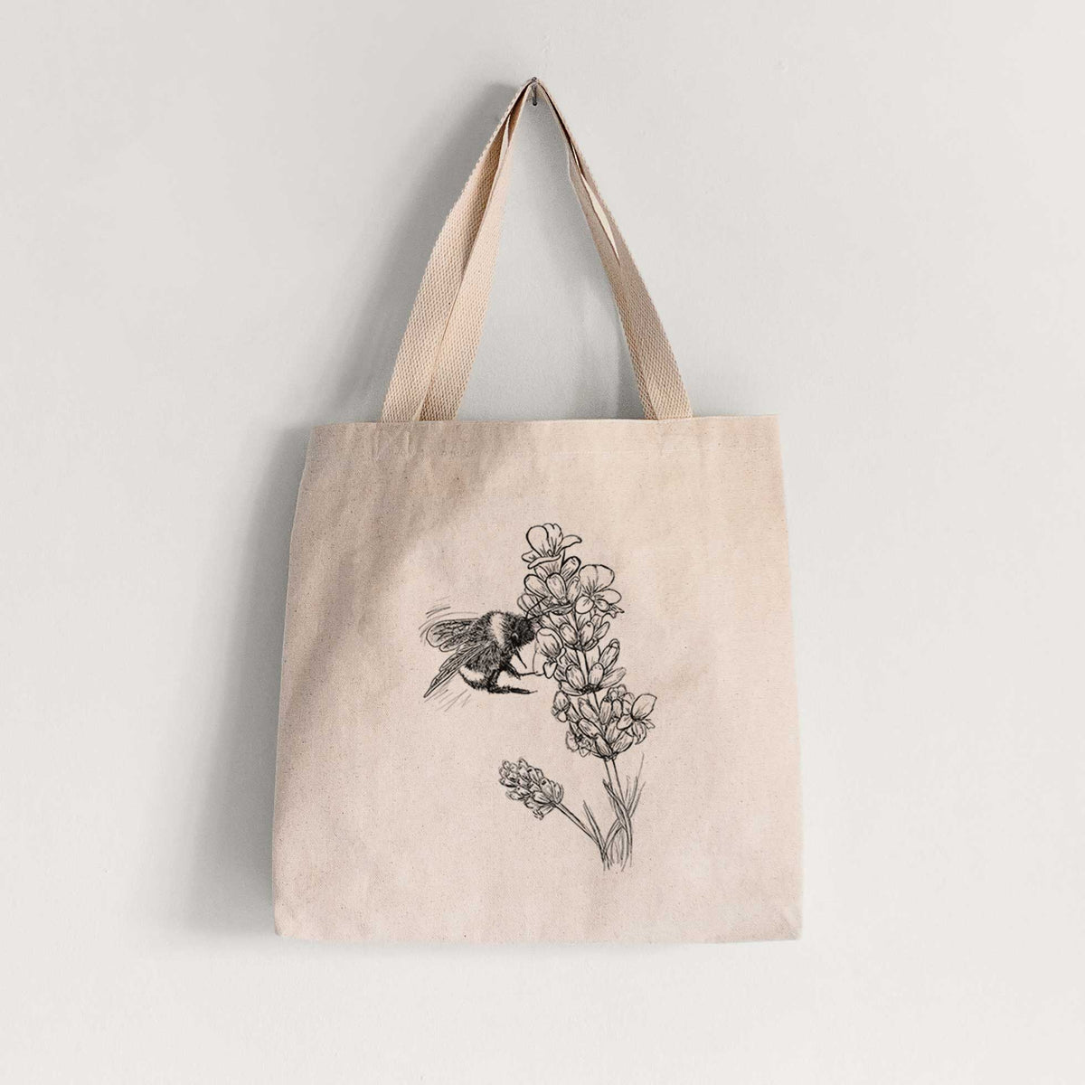 Natural canvas tote bag printed with a black ink illustration of a bumble bee visiting a sprig of lavender.