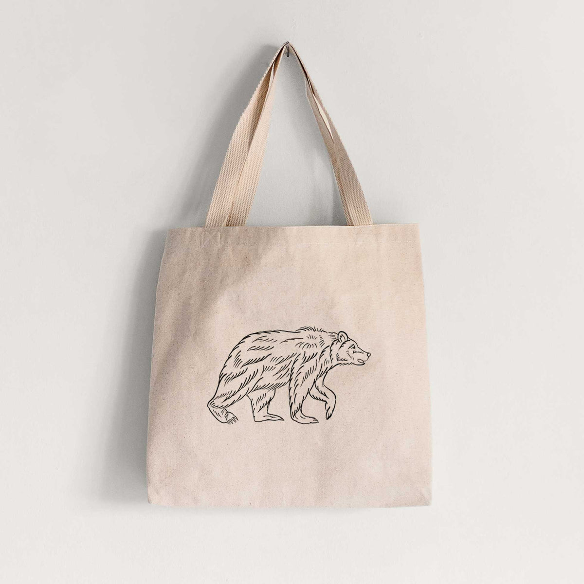 Natural canvas tote bag printed with a black ink illustration of a brown bear walking.