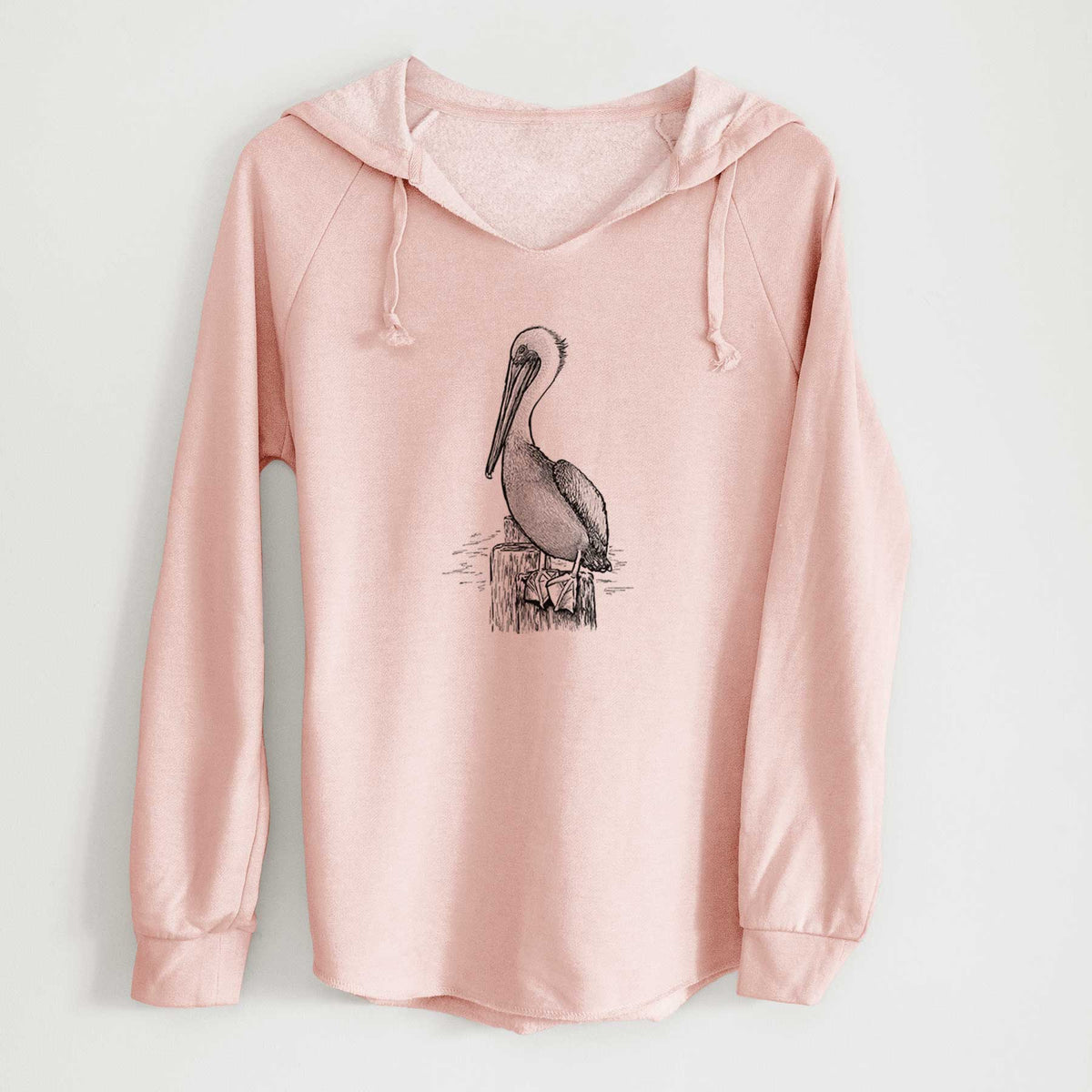 Blush pink women's Cali Wave hooded sweatshirt laid flat, printed with a detailed black ink illustration of a brown pelican perched on a wooden piling.