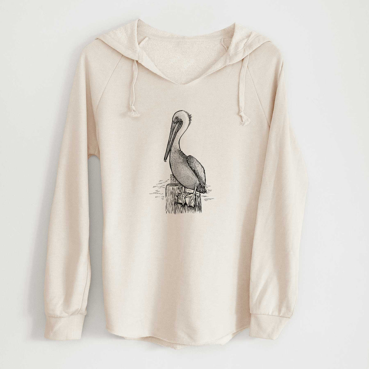 Bone cream women's Cali Wave hooded sweatshirt laid flat, printed with a detailed black ink illustration of a brown pelican perched on a wooden piling.