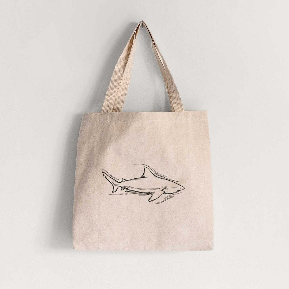 Natural canvas tote bag printed with a black ink illustration of a bull shark swimming.