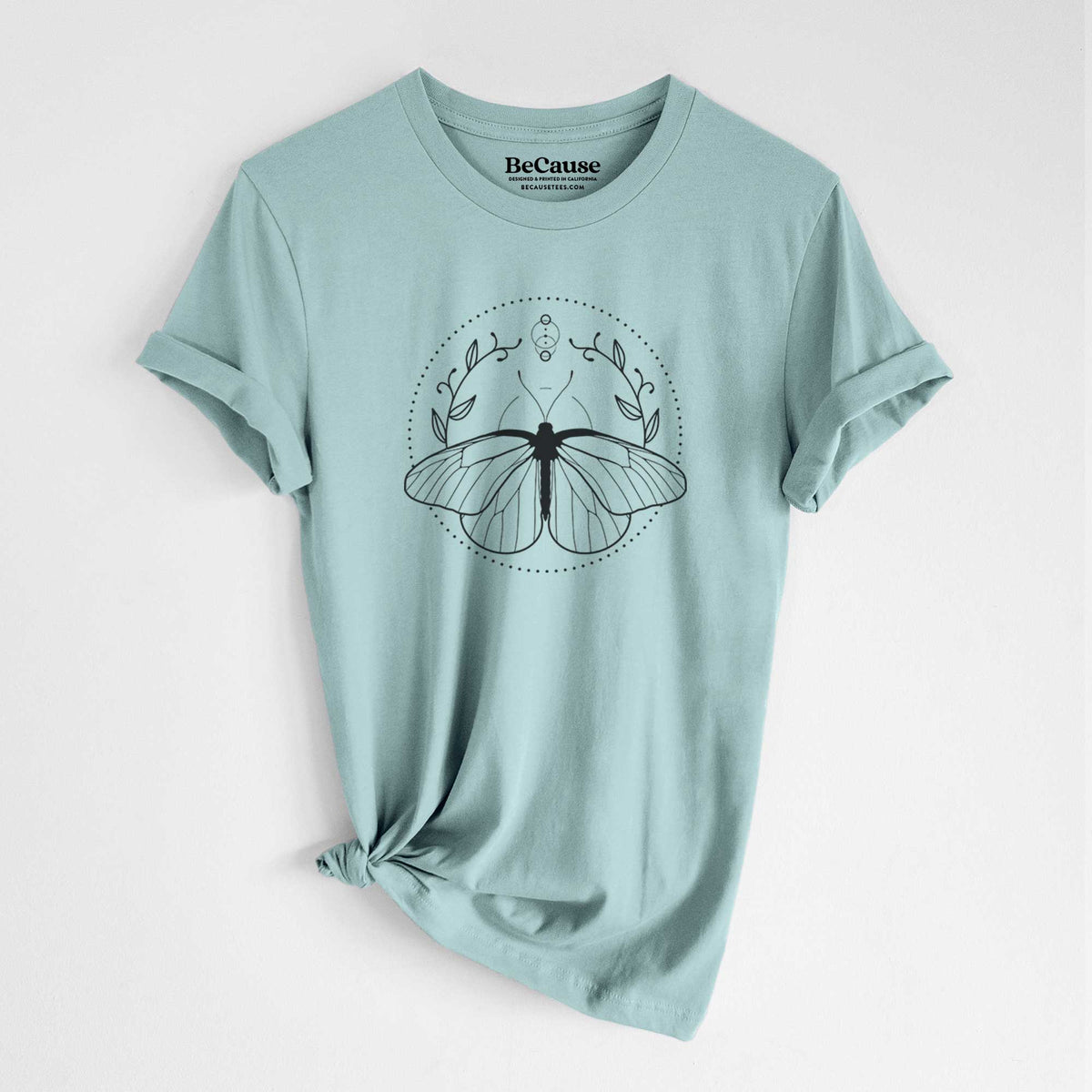 Dusty blue lightweight cotton t-shirt laid flat with the sleeves rolled, printed with a black ink butterfly inside a circle, framed by moon phases and leaves.