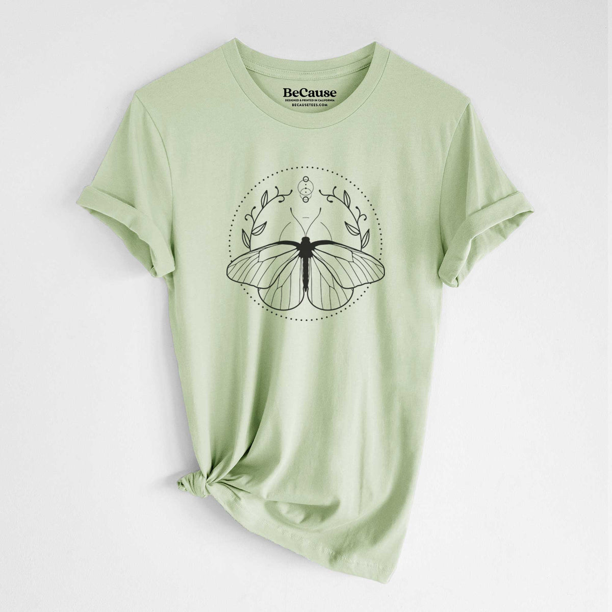 Spring green lightweight cotton t-shirt laid flat with the sleeves rolled, printed with a black ink butterfly inside a circle, framed by moon phases and leaves.