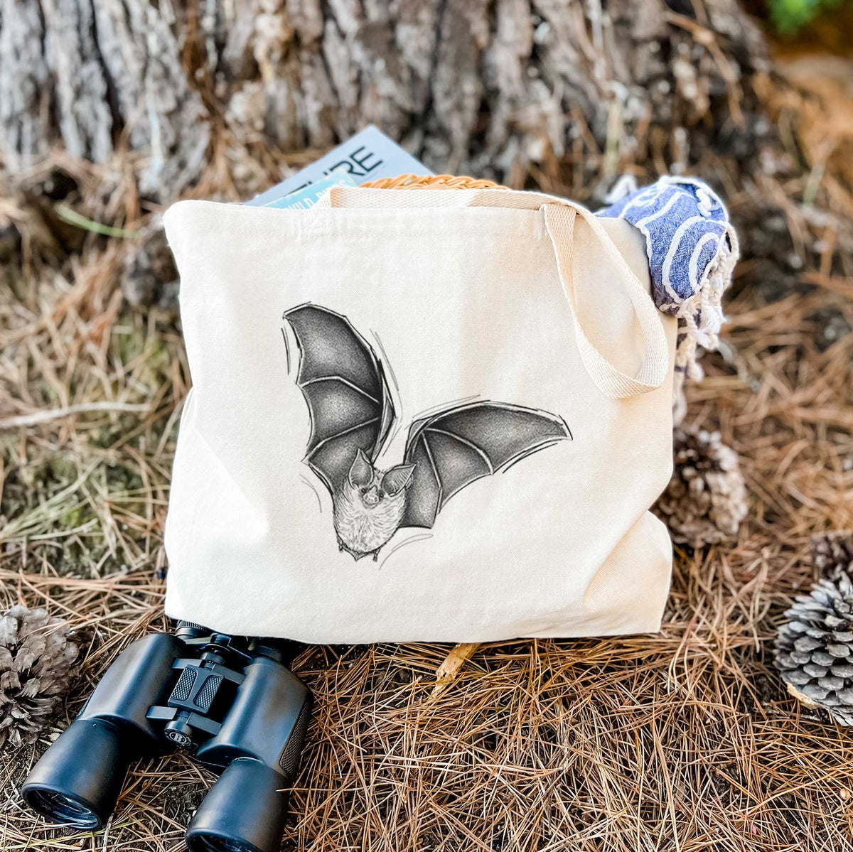 Canvas tote bag printed with a detailed black ink illustration of a California leaf-nosed bat in flight, resting on dry grass beside a pair of binoculars.