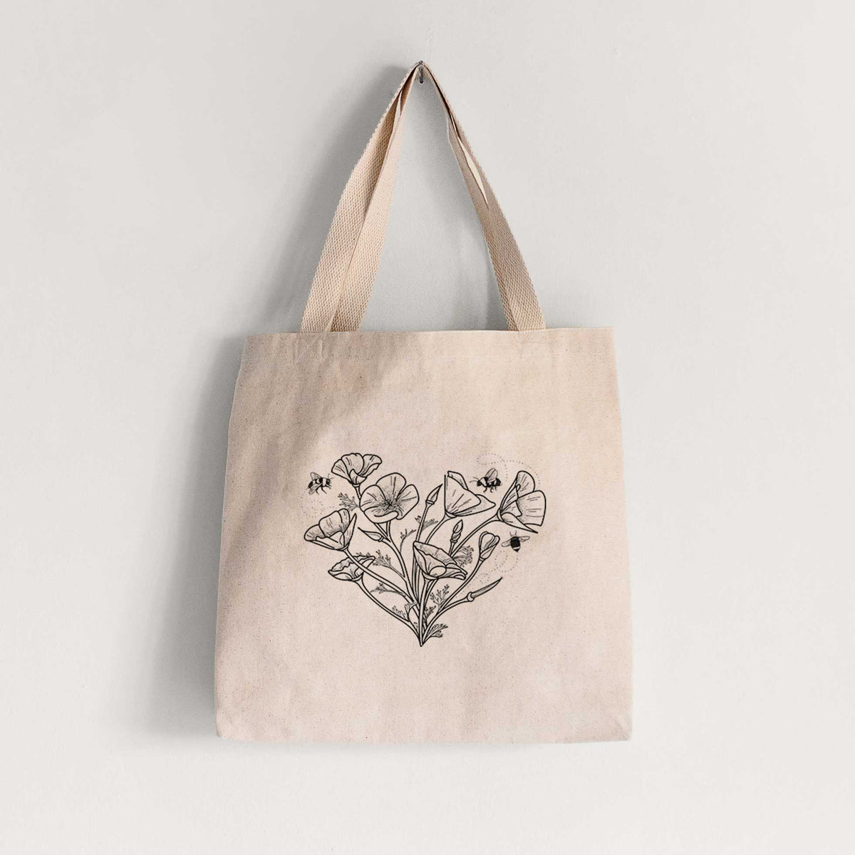 Natural canvas tote bag printed with a black ink line drawing of California poppies arranged in a heart shape, with small bees.
