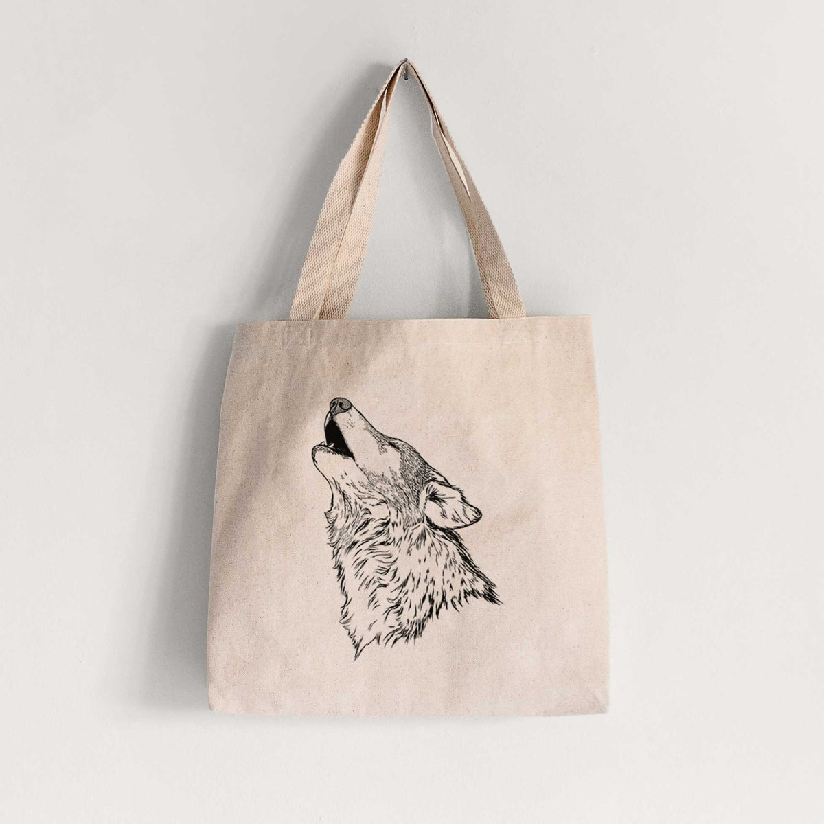 Natural canvas tote bag printed with a detailed black ink illustration of a grey wolf's head and shoulders, howling upward.
