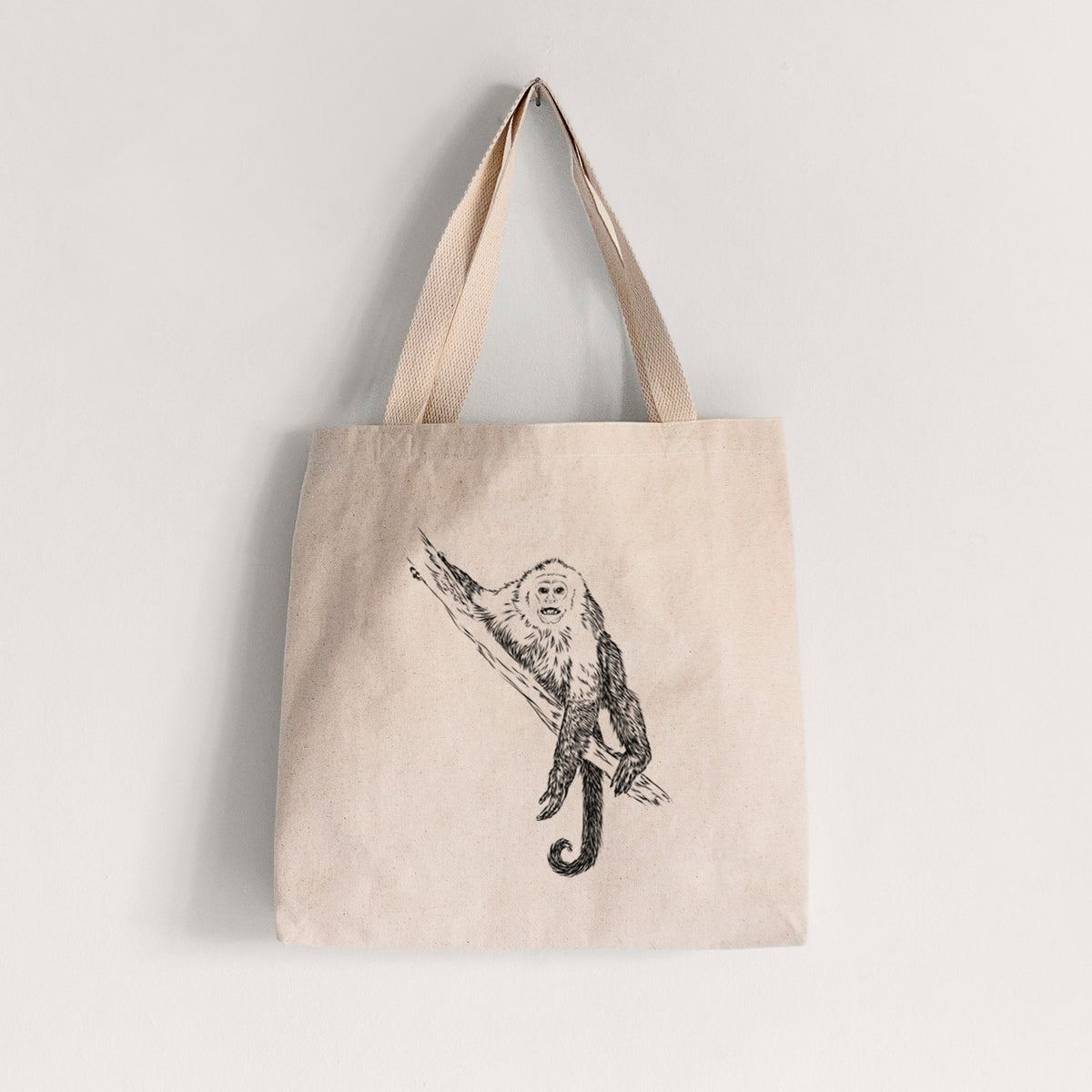 Natural canvas tote bag printed with a detailed black ink illustration of a capuchin monkey climbing a branch.