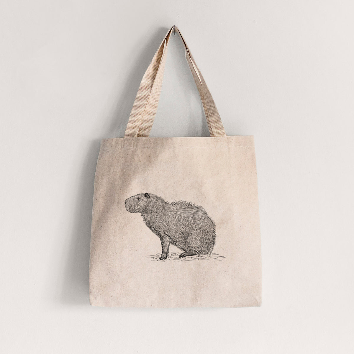 Natural canvas tote bag printed with a detailed black ink illustration of a capybara standing in profile.