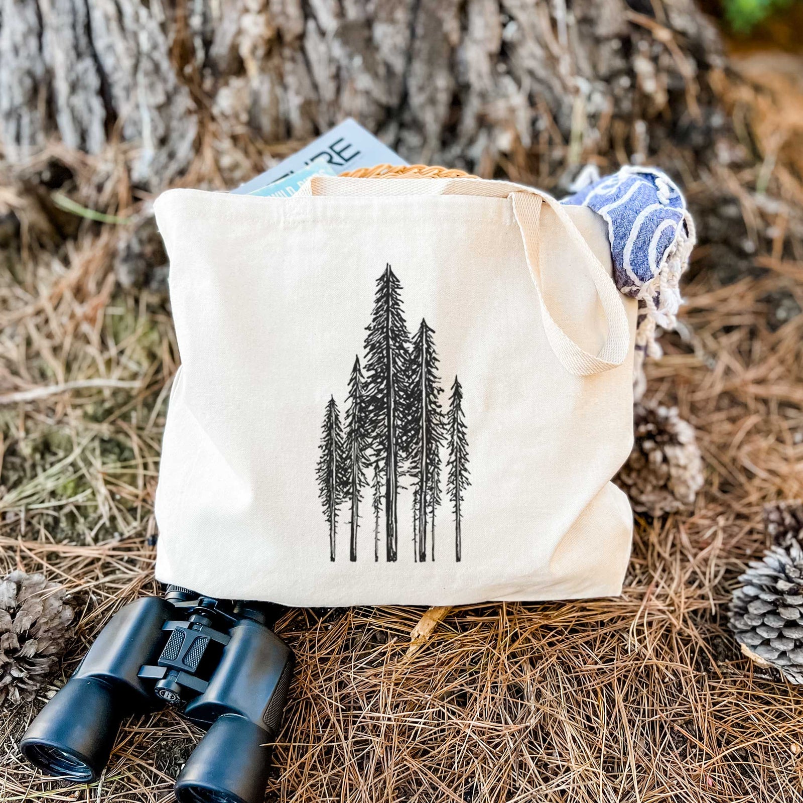 Natural canvas tote bag printed with a black ink illustration of a stand of tall coastal redwood trees with slender trunks and layered branches.