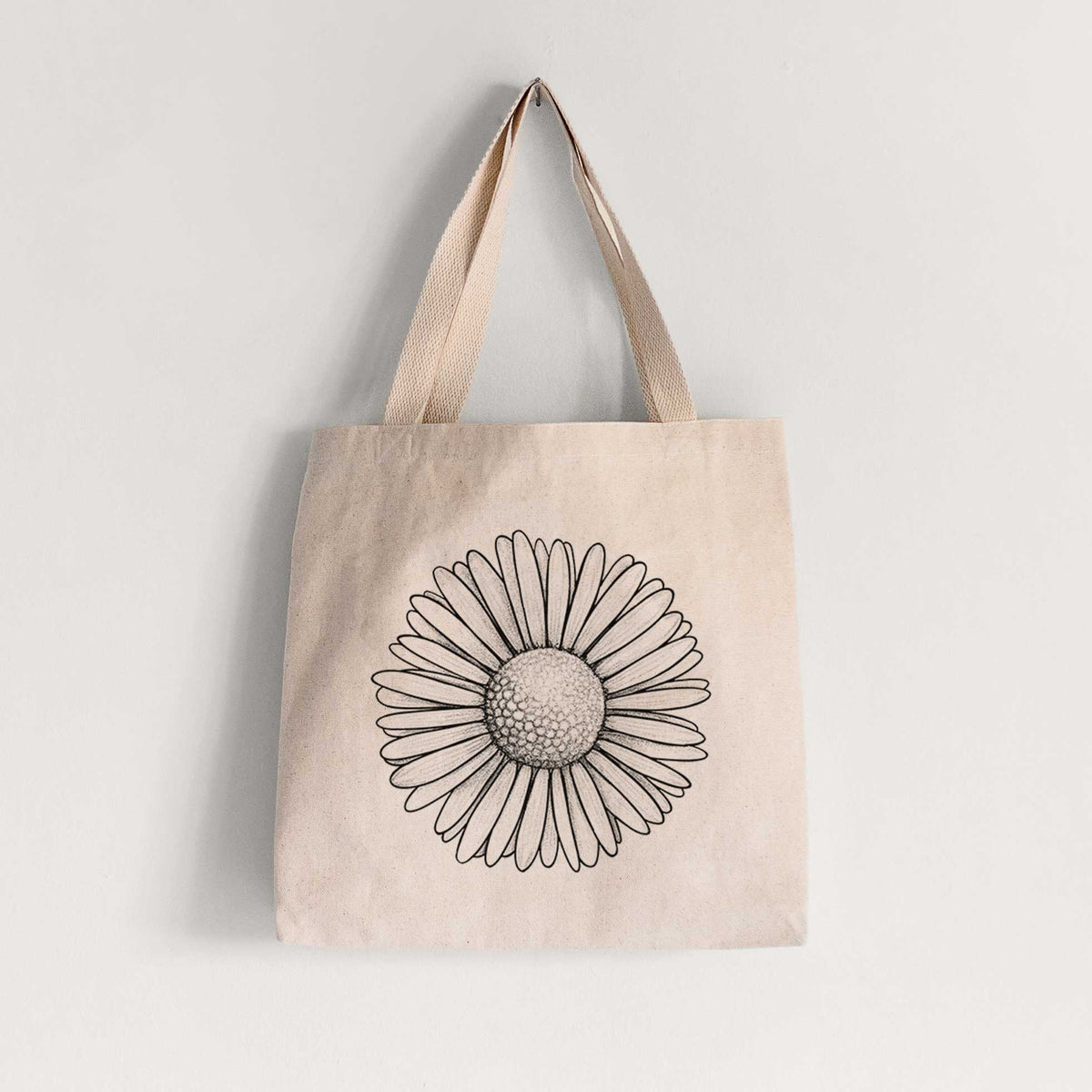 Natural canvas tote bag printed with a detailed black ink line drawing of a single common daisy flower.
