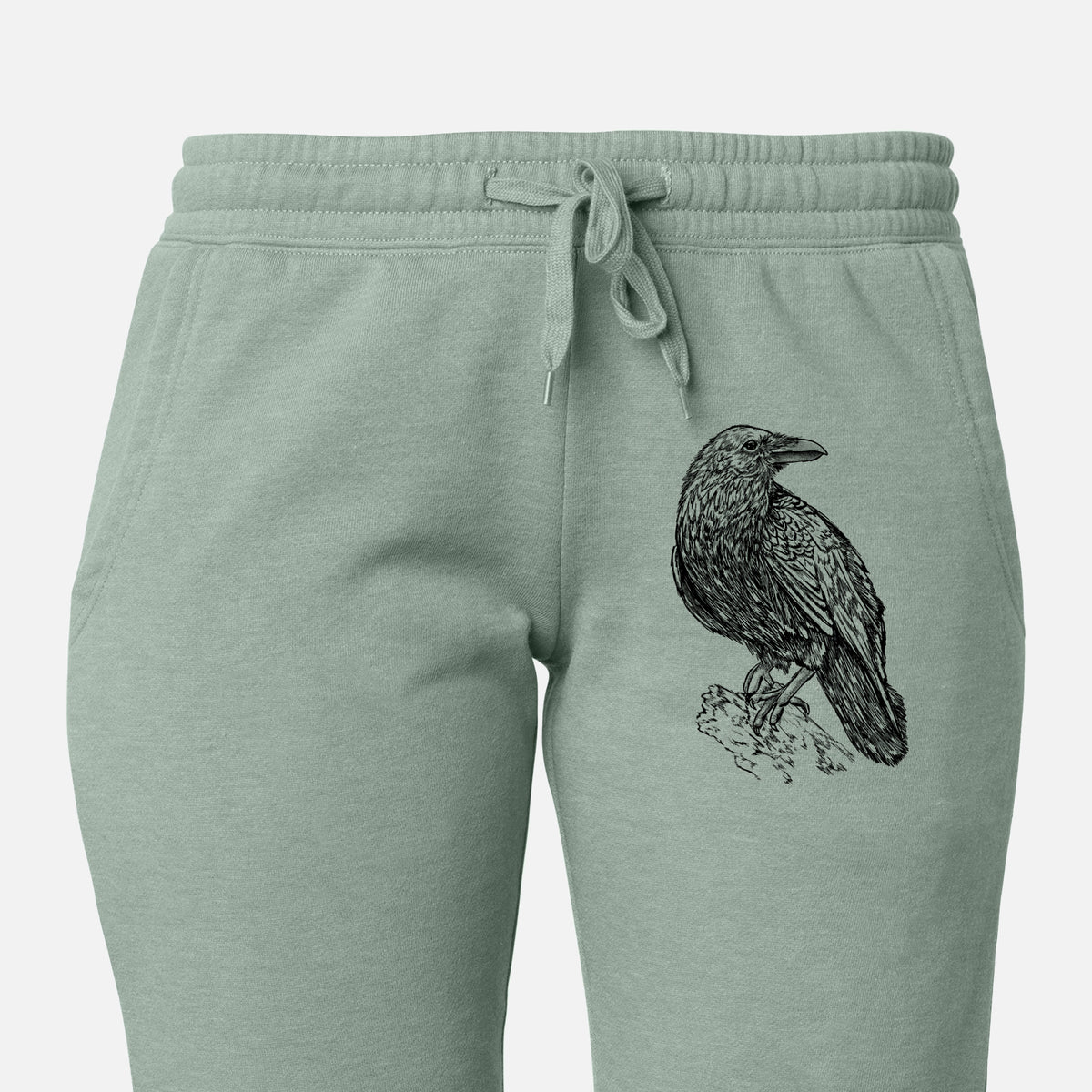 Front of sage green Cali Wave sweatpants, printed with a detailed black ink sketch of a common raven perched on a rock on the leg.