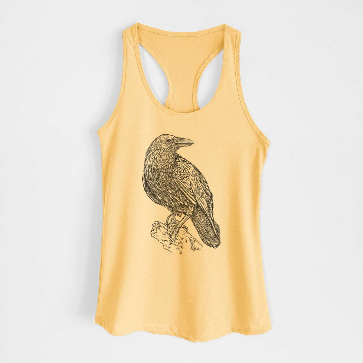 Banana cream women's racerback tank top laid flat, printed with a detailed black ink sketch of a common raven perched on a rock.