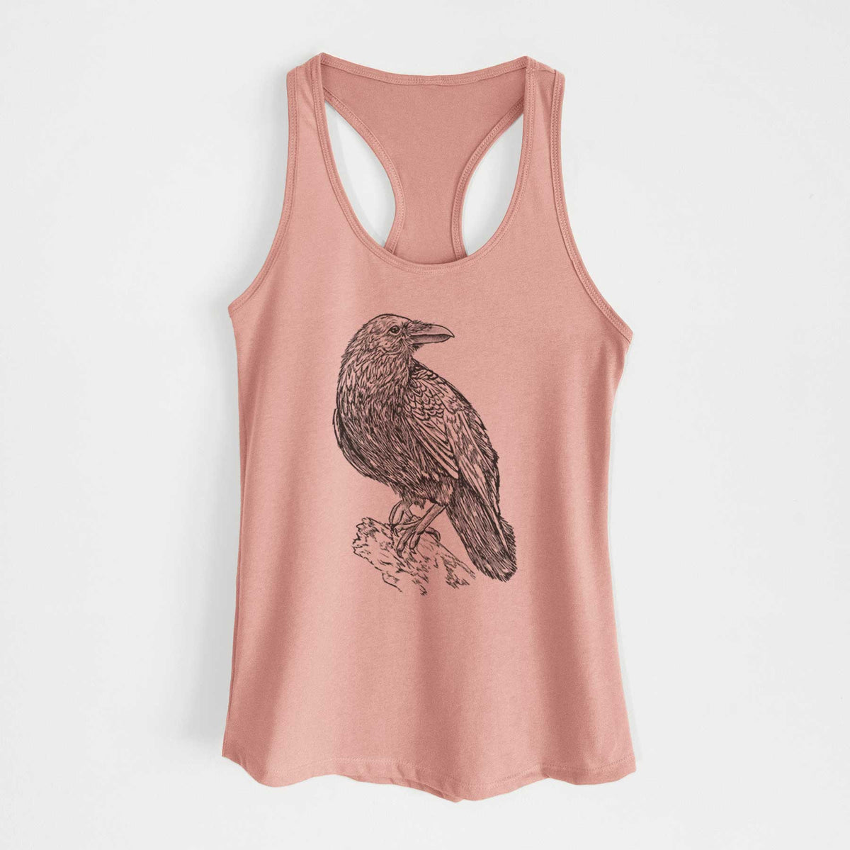 Desert pink women's racerback tank top laid flat, printed with a detailed black ink sketch of a common raven perched on a rock.