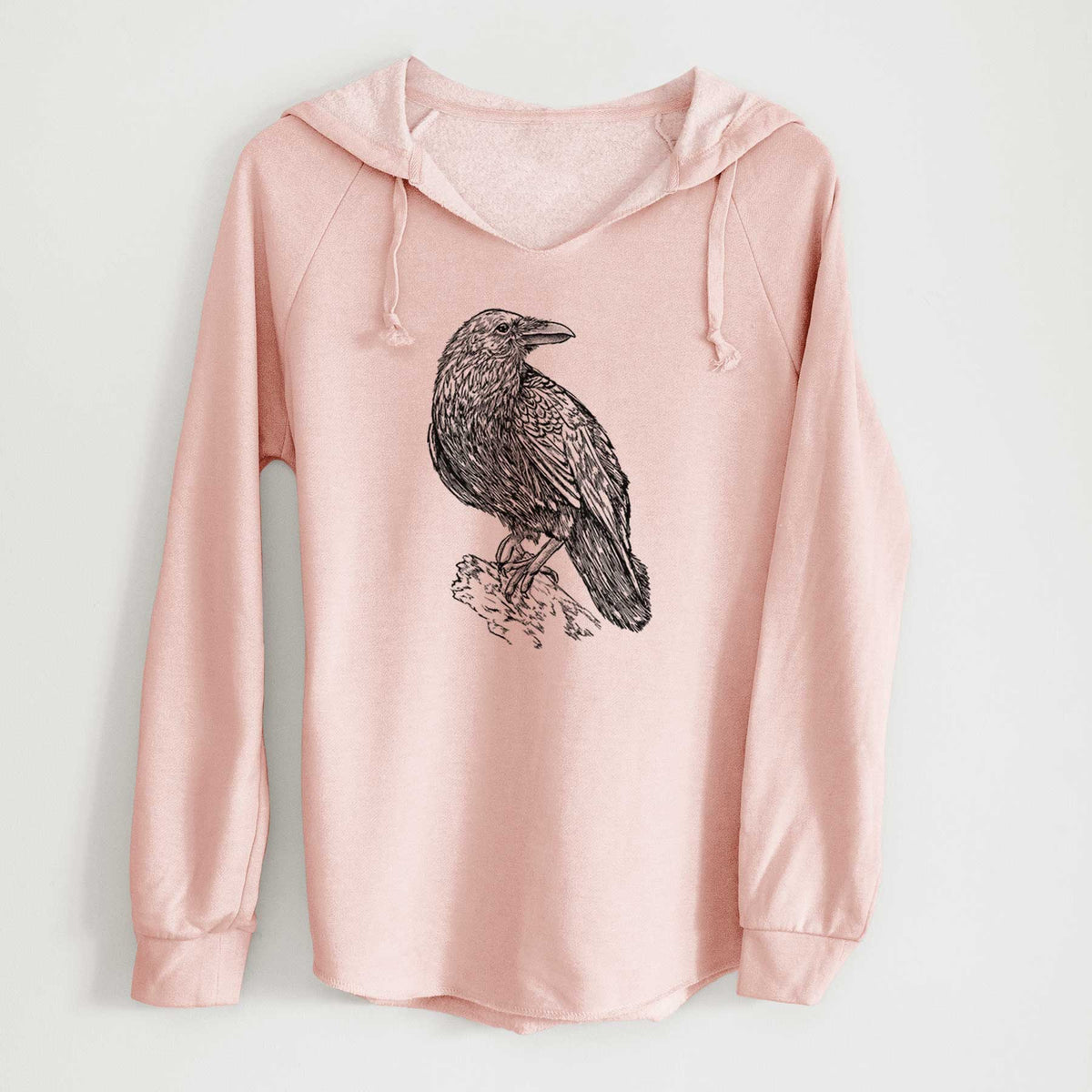 Blush pink women's Cali Wave hooded sweatshirt laid flat, printed with a detailed black ink sketch of a common raven perched on a rock.
