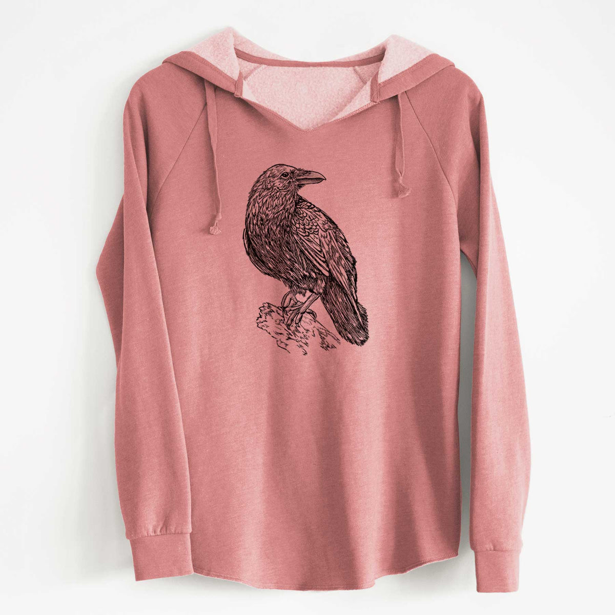 Dusty rose women's Cali Wave hooded sweatshirt laid flat, printed with a detailed black ink sketch of a common raven perched on a rock.