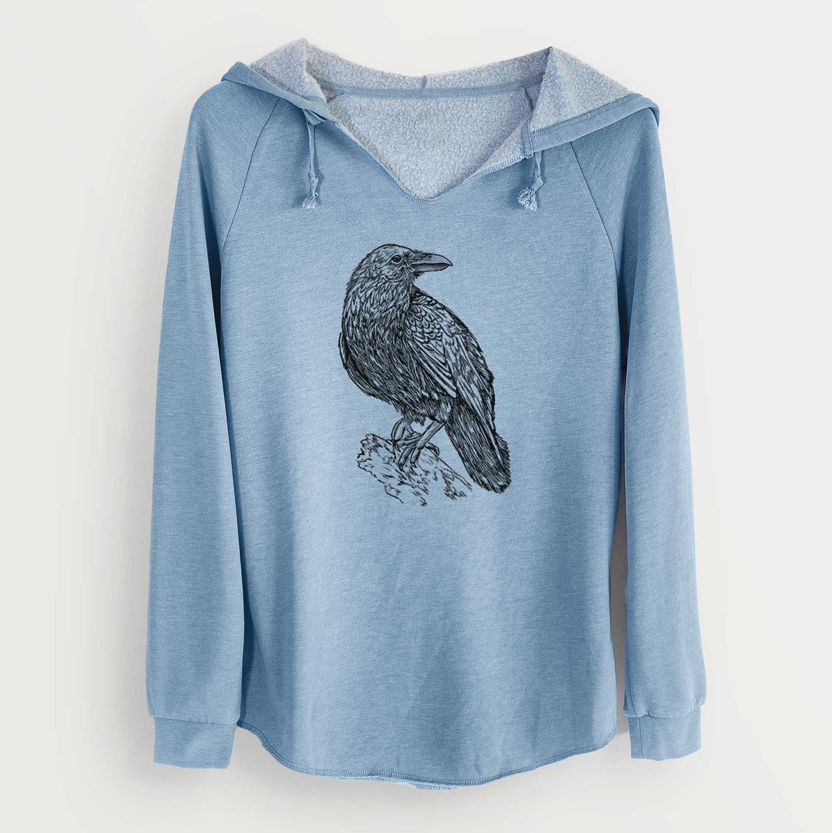 Misty blue women's Cali Wave hooded sweatshirt laid flat, printed with a detailed black ink sketch of a common raven perched on a rock.