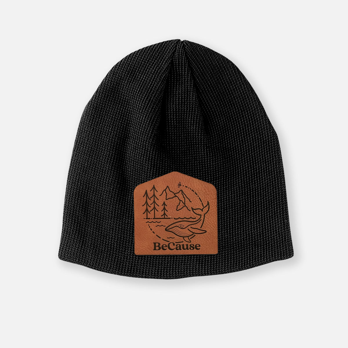 Black cotton beanie with a black line art circle connecting a mountain range, pine trees, a bee and a whale swimming in ocean waves on the front.