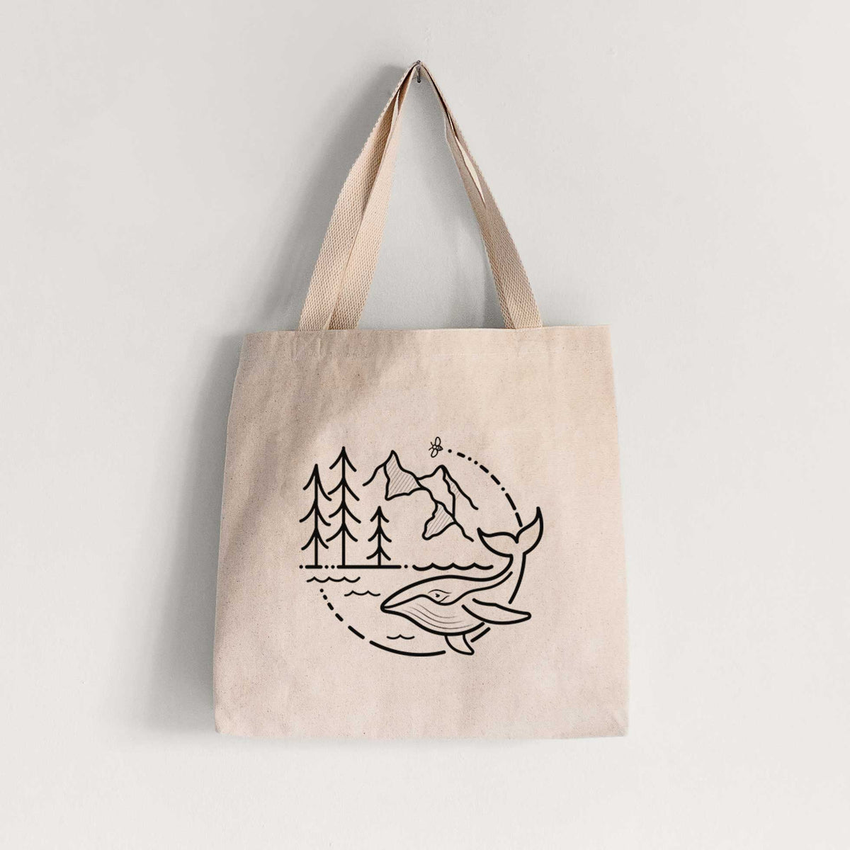 Natural canvas tote bag printed with a black line art circle connecting a mountain range, pine trees, a bee and a whale swimming in ocean waves.