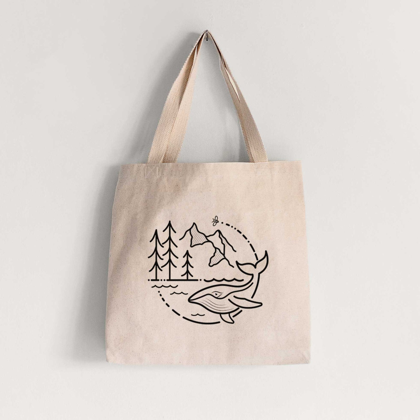 Natural canvas tote bag printed with a black line art circle connecting a mountain range, pine trees, a bee and a whale swimming in ocean waves.