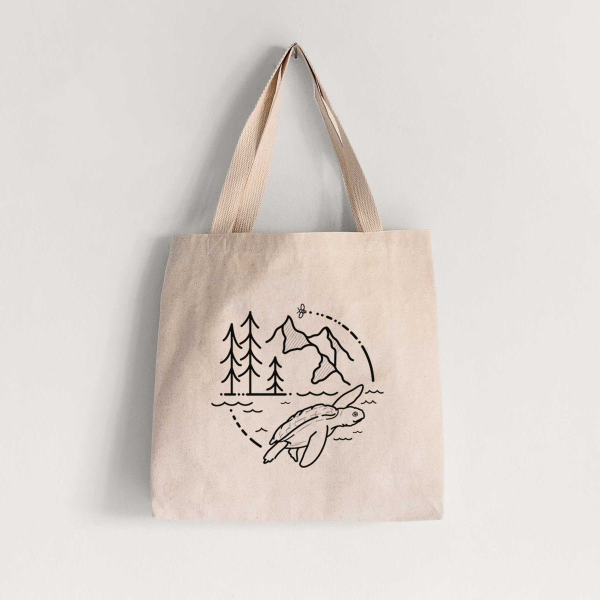 Natural canvas tote bag printed with a black line art circle connecting pine trees, mountains, a bee and a Kemp's ridley sea turtle swimming.