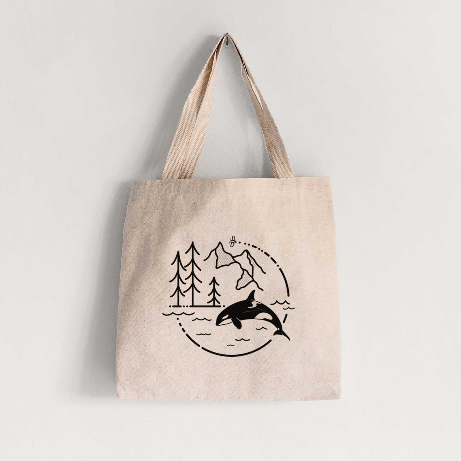 Natural canvas tote bag printed with a black line art circle connecting pine trees, mountains, a bee and an orca leaping from ocean waves.