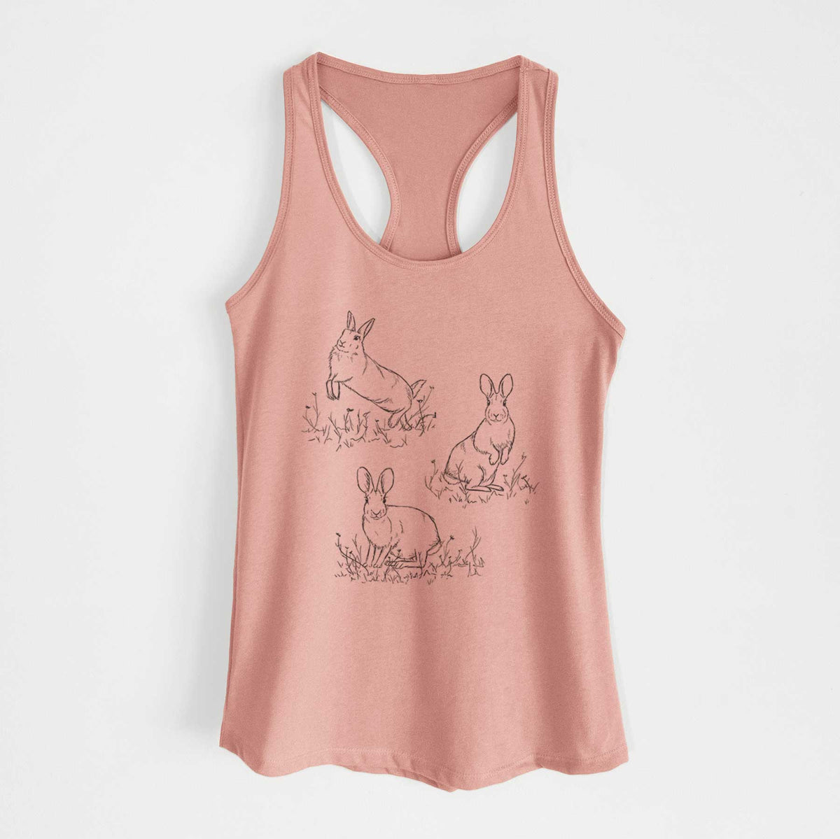Desert pink women's racerback tank top laid flat, printed with a black ink illustration of three cottontail rabbits among grass and flowers.