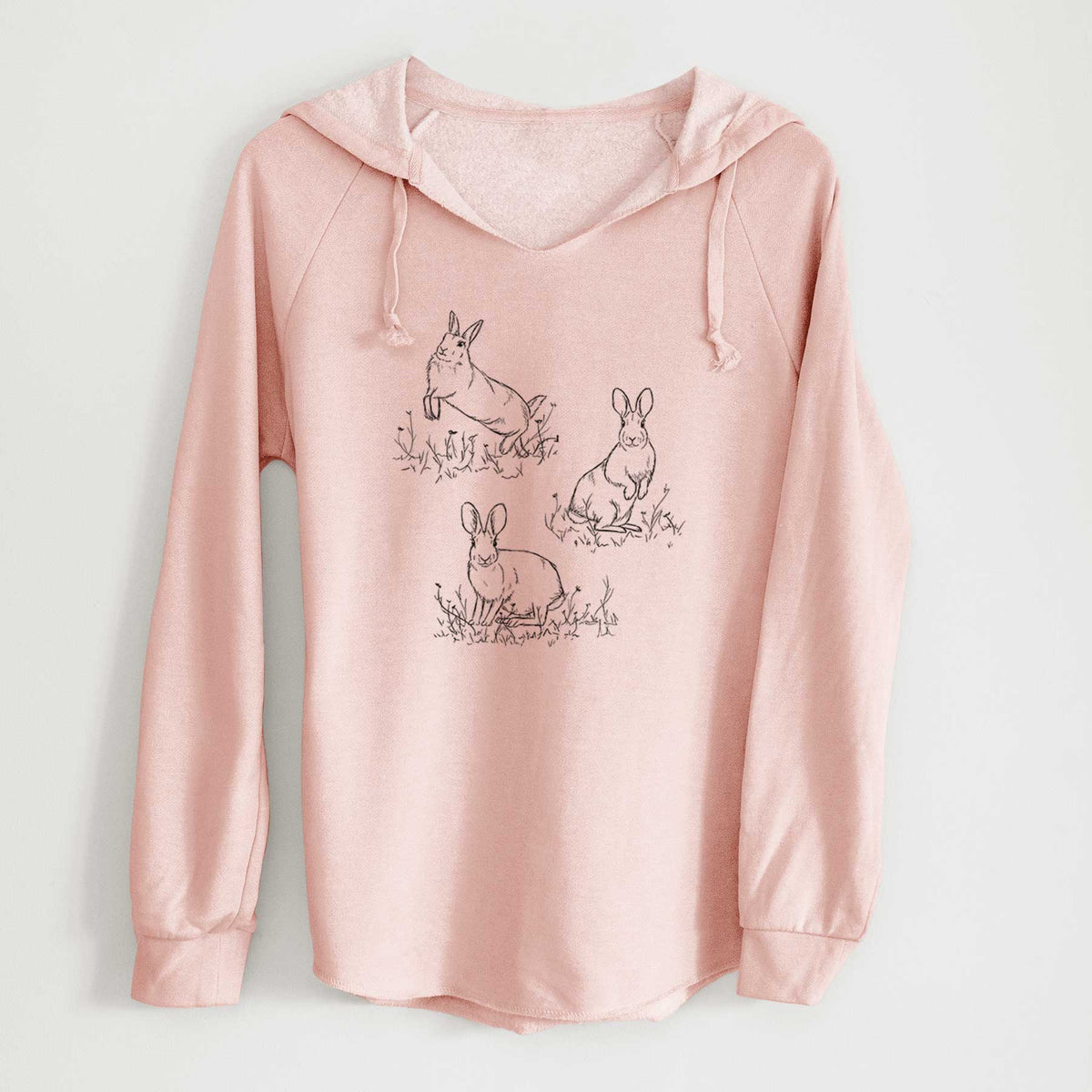 Blush pink women's Cali Wave hooded sweatshirt laid flat, printed with a black ink illustration of three cottontail rabbits among grass and flowers.