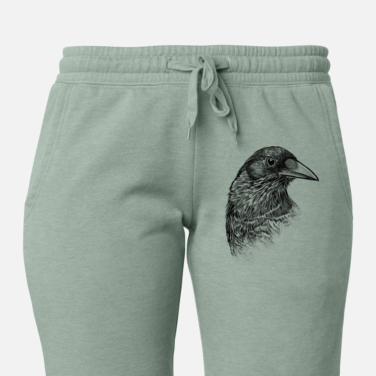 Front of sage green Cali Wave sweatpants, printed with a detailed black ink portrait of a crow's head in profile on the leg.