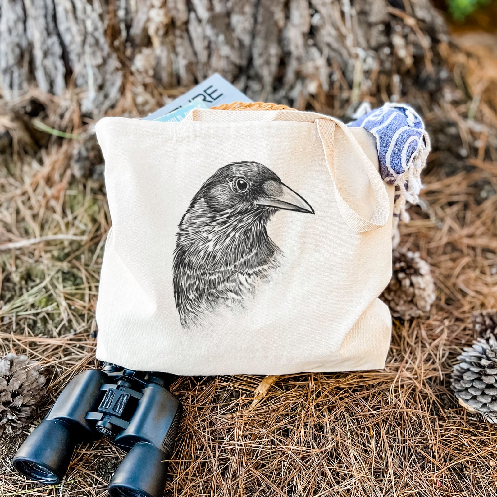 Natural canvas tote bag printed with a detailed black ink portrait of a crow's head in profile.