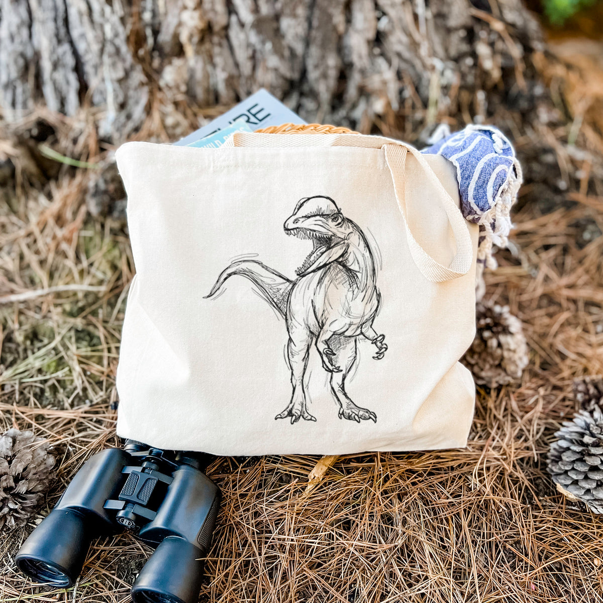 Canvas tote bag printed with a black ink illustration of a Dilophosaurus with its neck frill, walking, resting on dry grass beside a pair of binoculars.