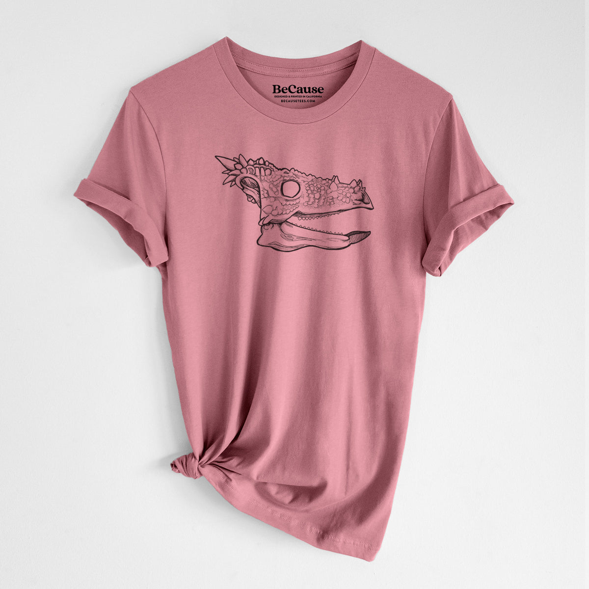 Mauve pink lightweight cotton t-shirt laid flat with the sleeves rolled, printed with a black ink illustration of a spiky Dracorex dinosaur skull.