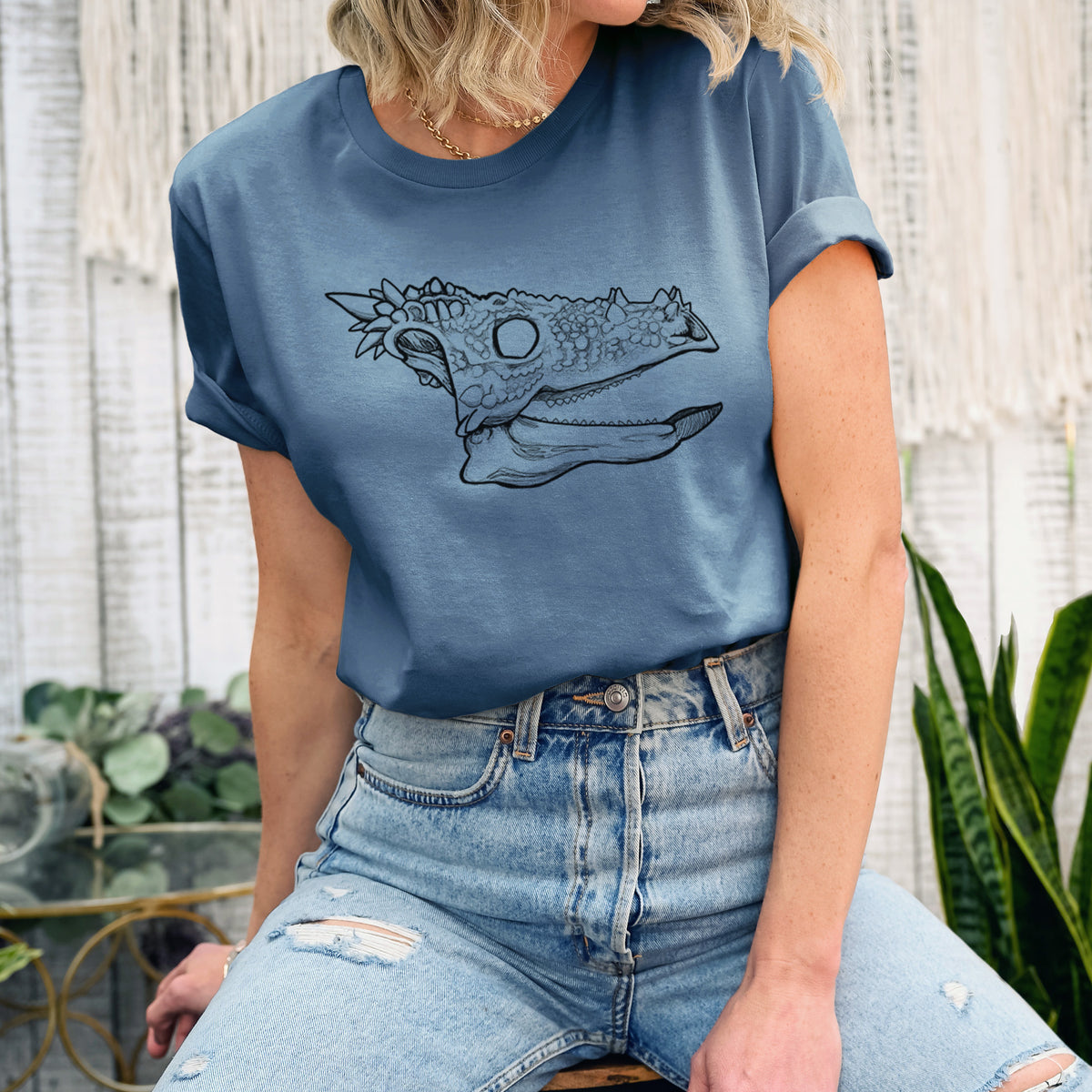 Woman wearing a steel blue lightweight cotton t-shirt printed with a black ink illustration of a spiky Dracorex dinosaur skull.