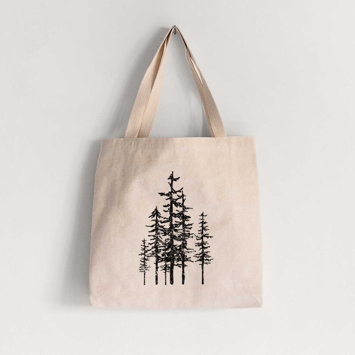 Natural canvas tote bag printed with a black ink illustration of a cluster of evergreen trees of varying heights.