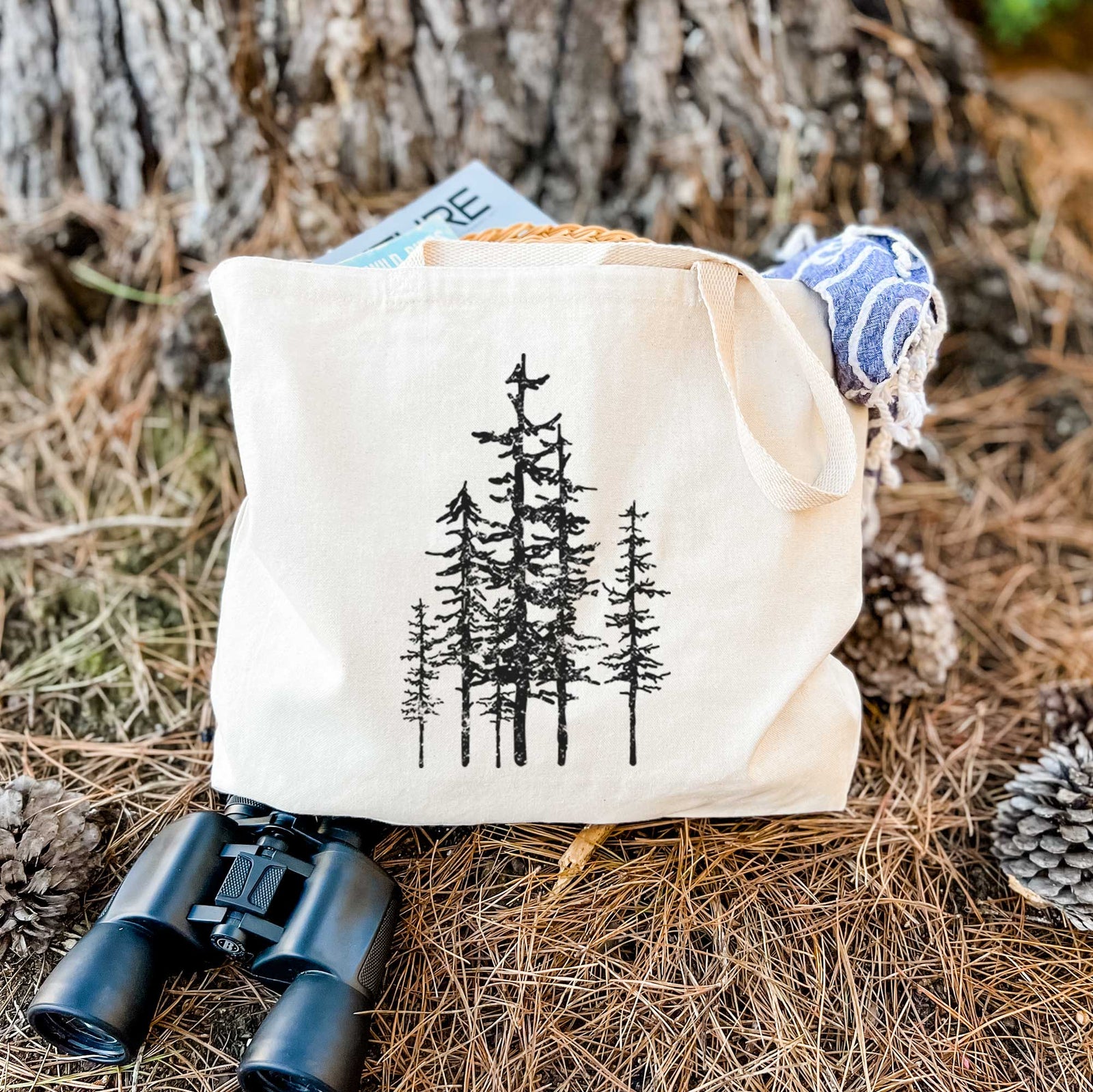 Natural canvas tote bag printed with a black ink illustration of a cluster of evergreen trees of varying heights.