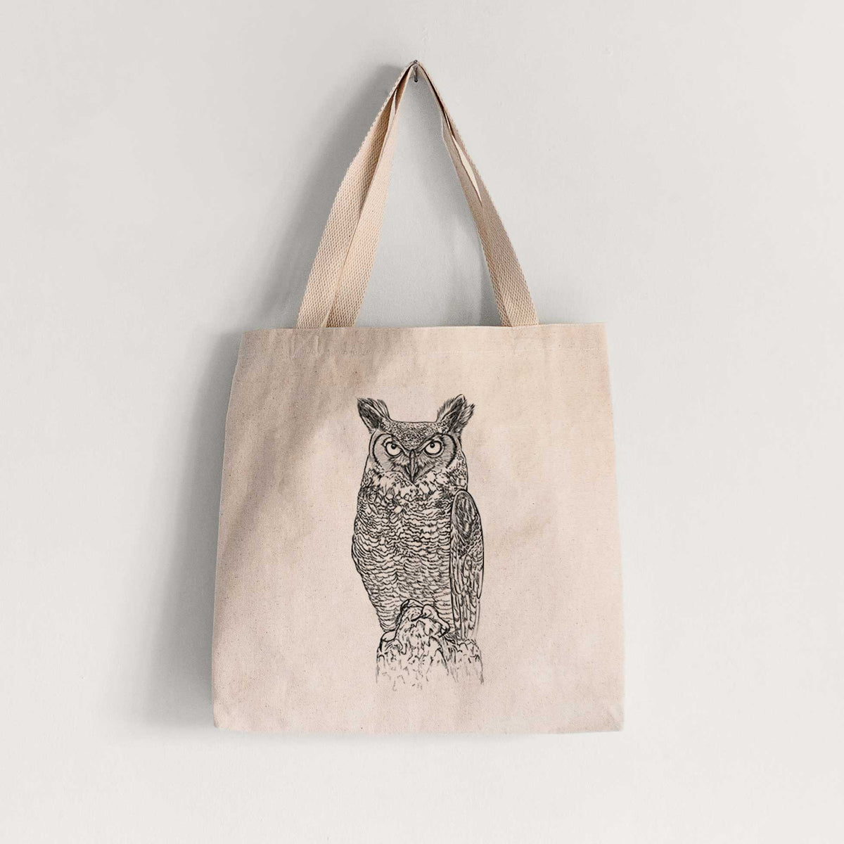 Natural canvas tote bag printed with a detailed black ink illustration of a great horned owl standing upright with its ear tufts raised.