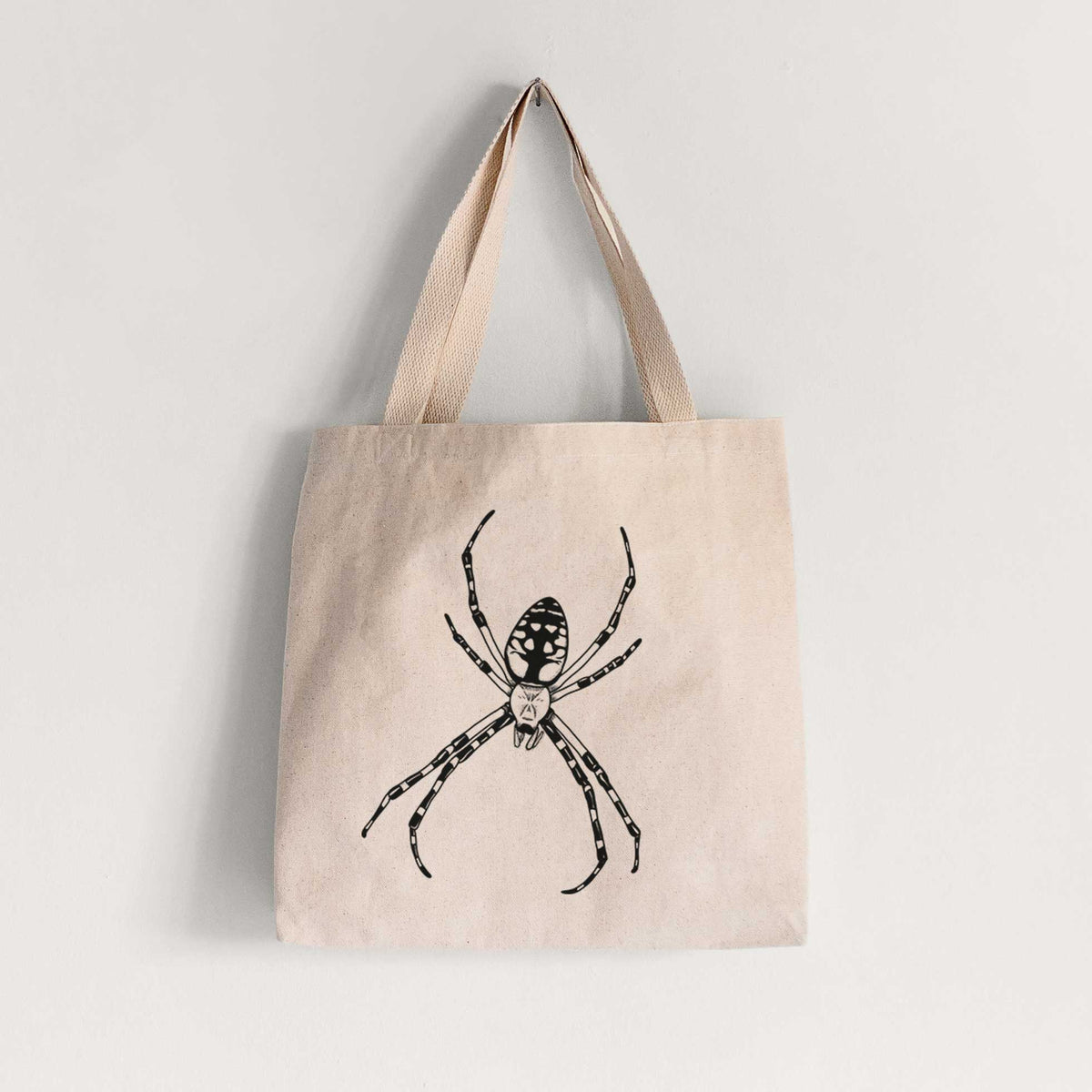 Natural canvas tote bag printed with a detailed black ink illustration of a garden spider with long striped legs.