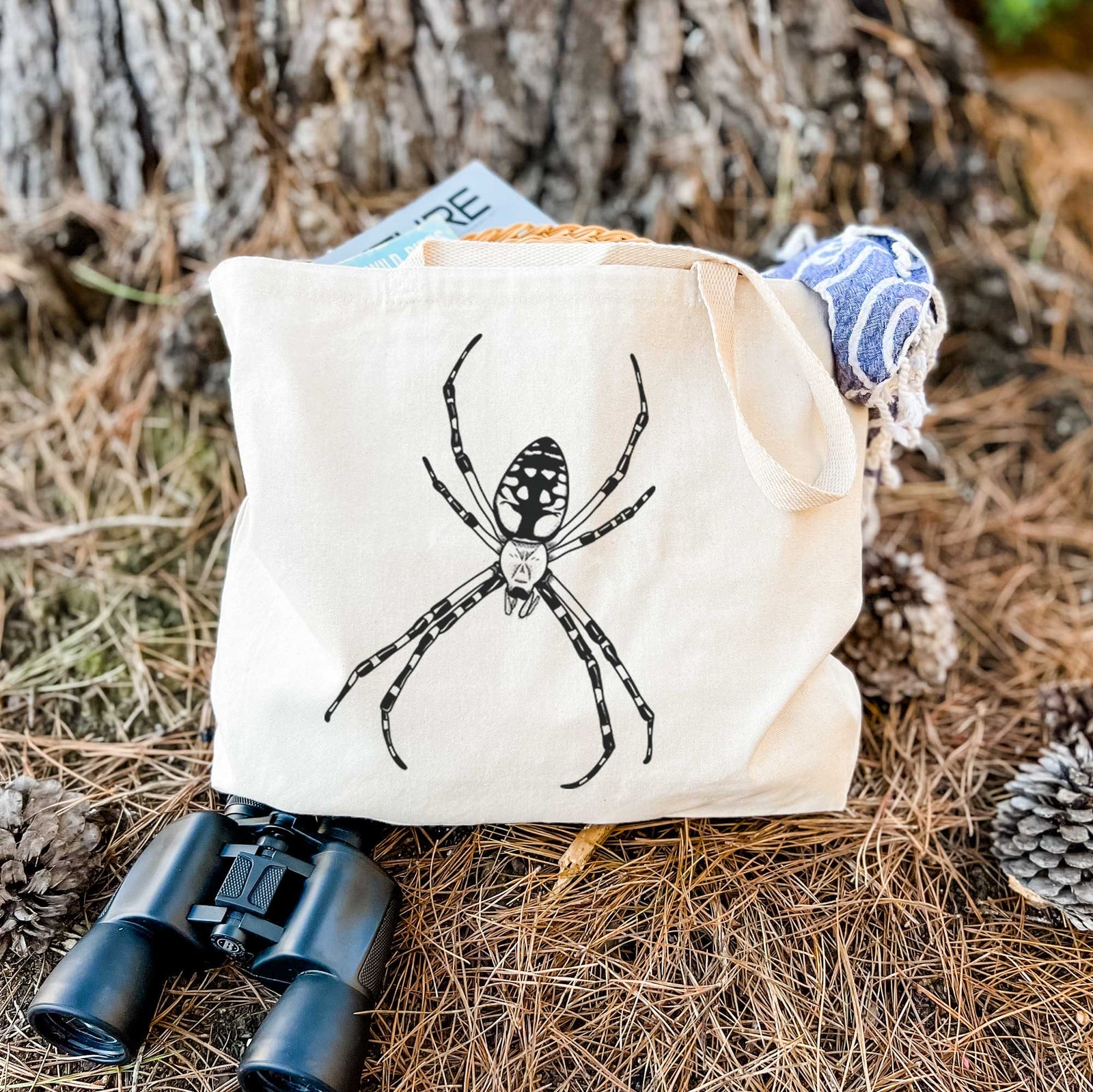 Natural canvas tote bag printed with a detailed black ink illustration of a garden spider with long striped legs.