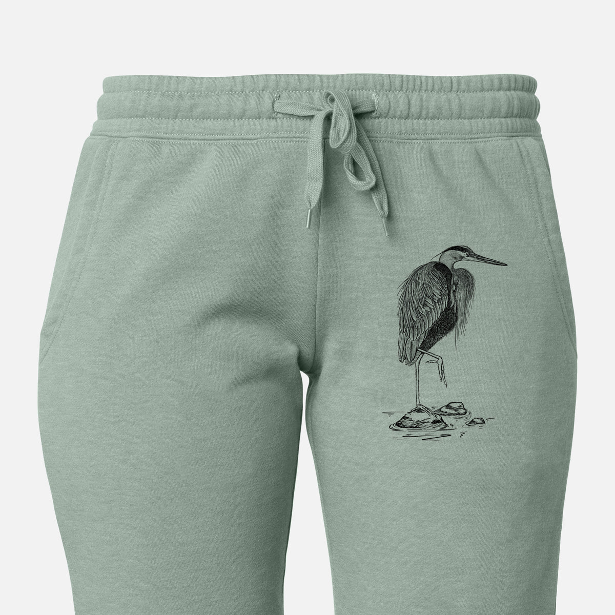 Front of sage green Cali Wave sweatpants, printed with a detailed black ink illustration of a great blue heron standing on rocks on the leg.