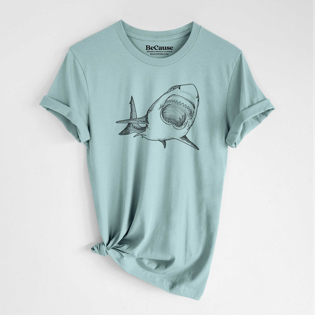 Dusty blue lightweight cotton t-shirt laid flat with the sleeves rolled, printed with a black ink illustration of a great white shark swimming toward the viewer with its mouth open.