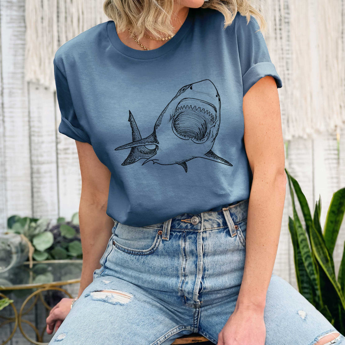 Woman wearing a steel blue lightweight cotton t-shirt printed with a black ink illustration of a great white shark swimming toward the viewer with its mouth open.