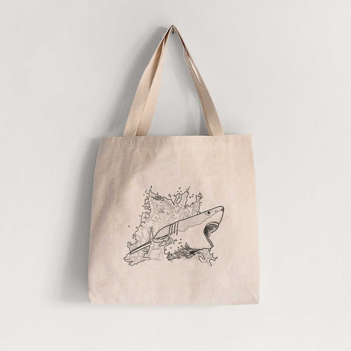 Natural canvas tote bag printed with a black ink illustration of a great white shark breaking through a splash of water.