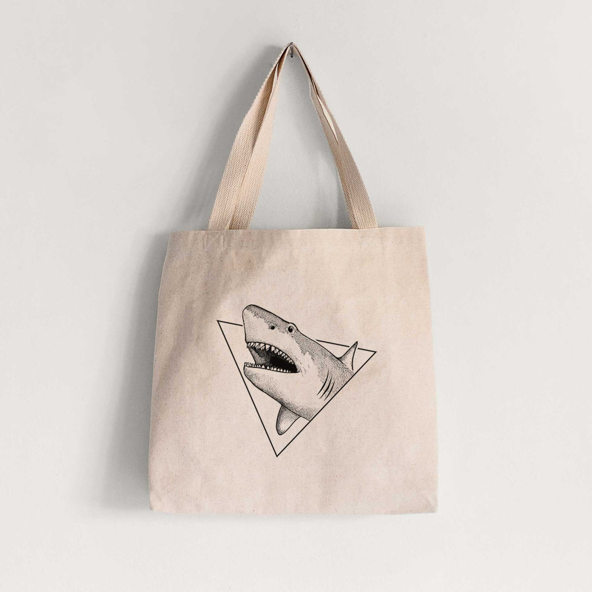 Natural canvas tote bag printed with a black ink great white shark bursting out of a triangle outline with its mouth open.