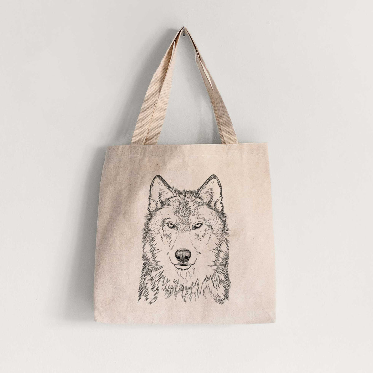 Natural canvas tote bag printed with a detailed black ink portrait of a grey wolf facing forward.