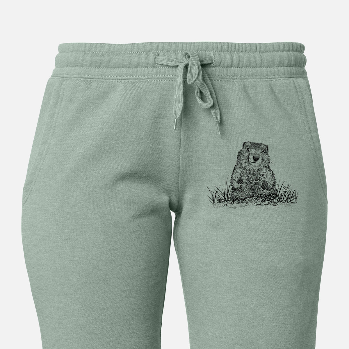 Front of sage green Cali Wave sweatpants, printed with a black ink illustration of a groundhog peeking out of its burrow among grass on the leg.