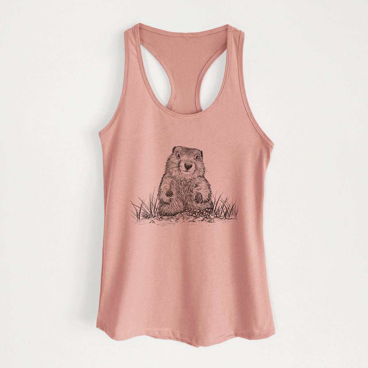 Desert pink women's racerback tank top laid flat, printed with a black ink illustration of a groundhog peeking out of its burrow among grass.