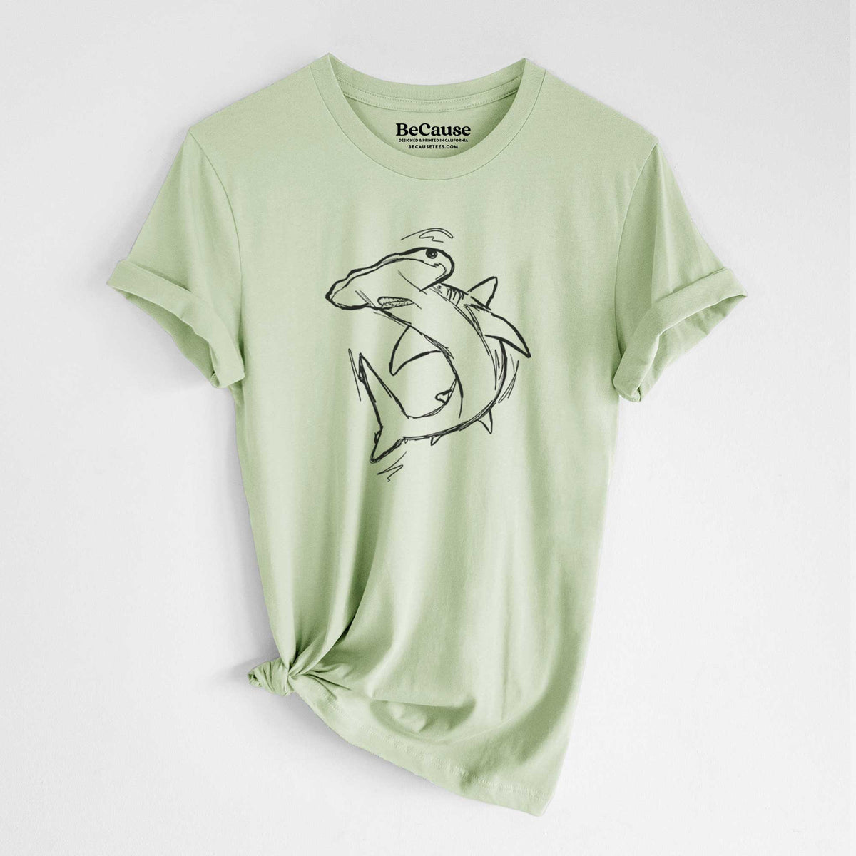 Spring green lightweight cotton t-shirt laid flat with the sleeves rolled, printed with a black ink illustration of a hammerhead shark swimming in a curve.