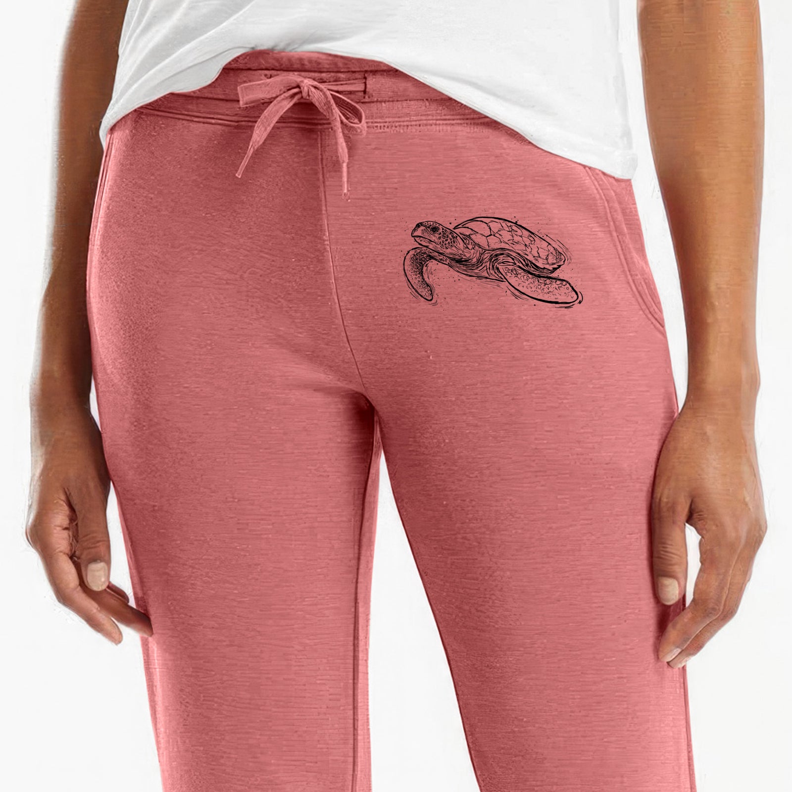 Front of dusty rose Cali Wave sweatpants, printed with a black ink illustration of a hawksbill sea turtle swimming, with a patterned shell on the leg.